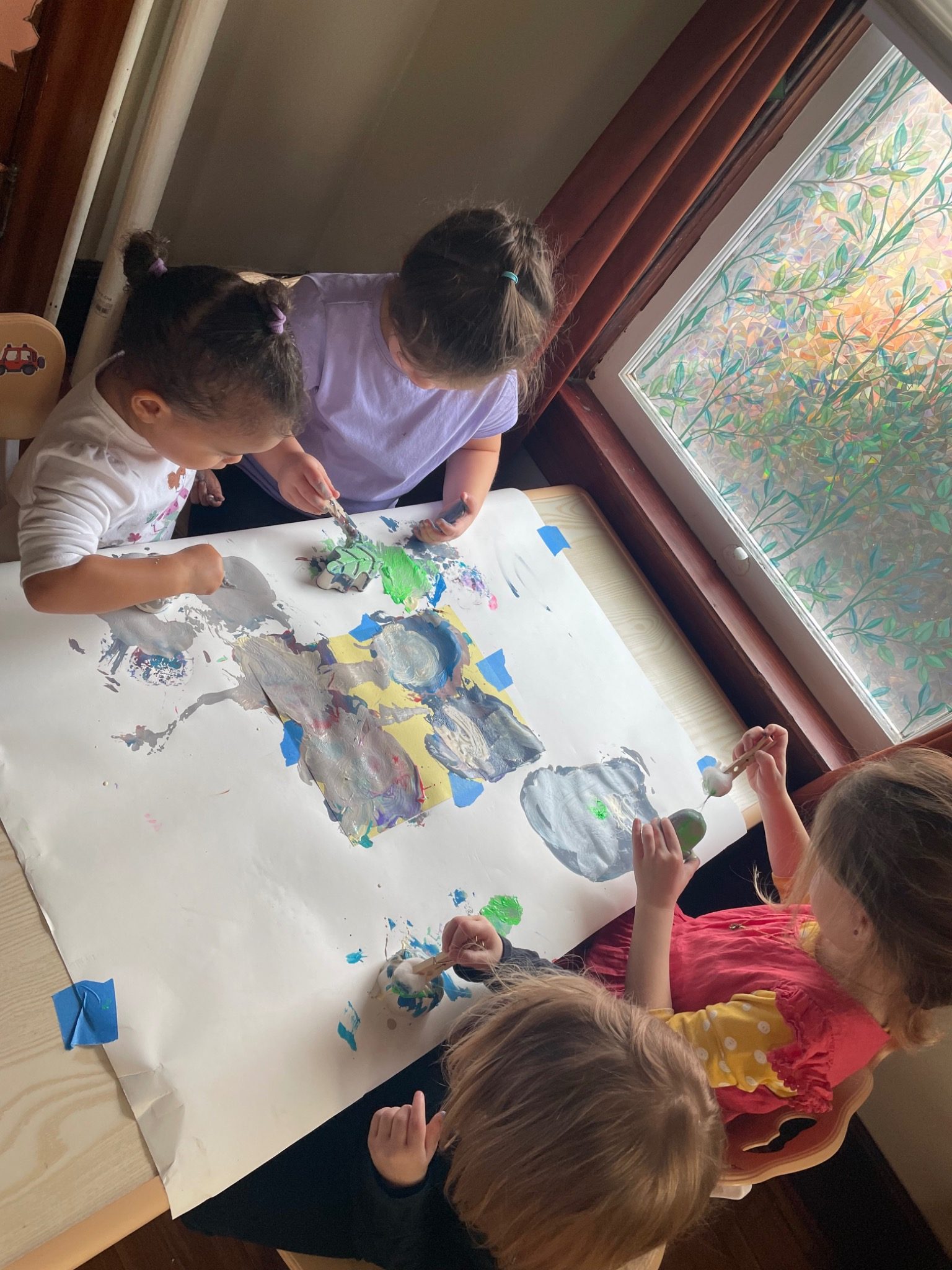 Children painting together at a table, viewed from above