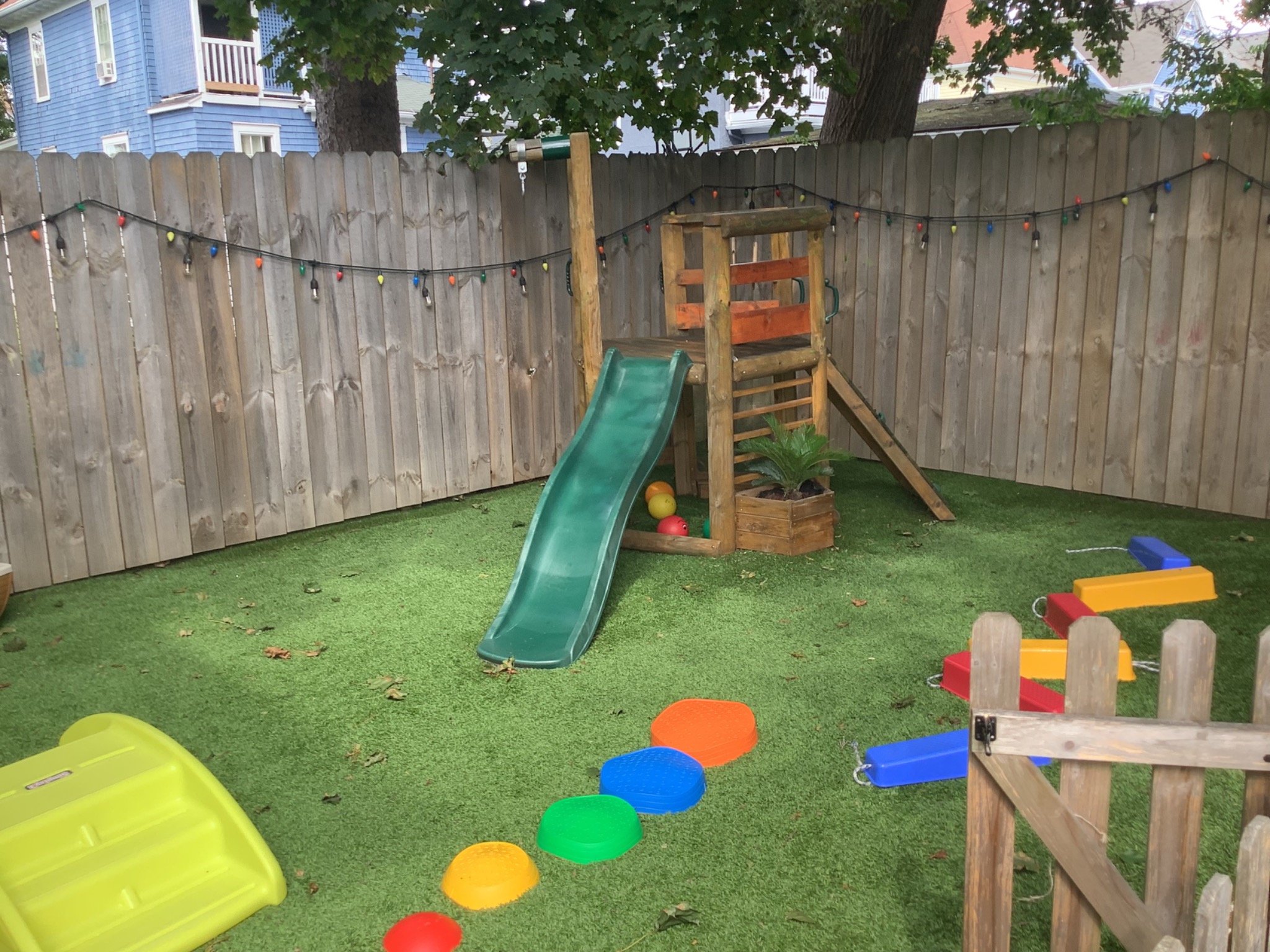 Wooden climbing structure and green slide in the fenced playground